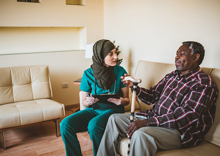 healthcare worker talking to elderly gentleman on couch